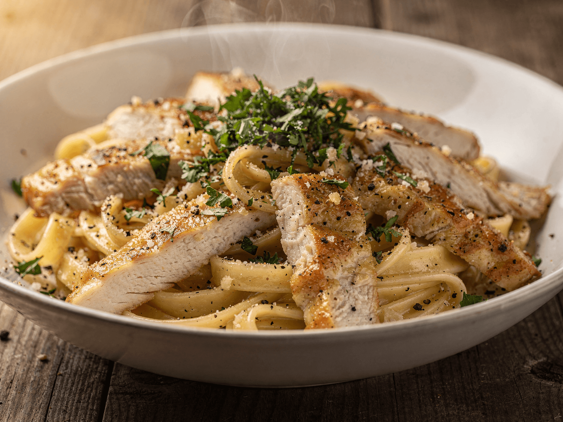 Close-up of creamy garlic Parmesan pasta with sliced chicken served in a bowl, garnished with fresh parsley and black pepper.