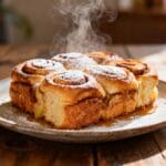 Fluffy Hawaiian roll French toast bake dusted with powdered sugar and drizzled with maple syrup on a rustic wooden table.