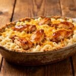 Cast iron skillet filled with creamy mac and cheese topped with honey garlic butter chicken and crispy breadcrumbs.