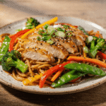 Chicken noodle stir fry with juicy sliced chicken breast, colorful vegetables, and glossy stir fry noodles on a plate.