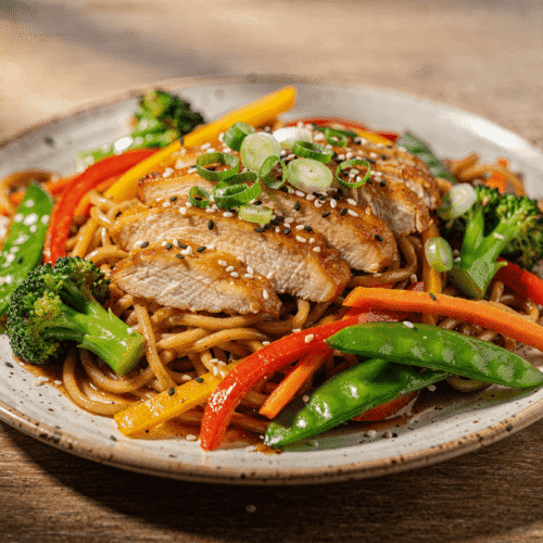 Chicken noodle stir fry with juicy sliced chicken breast, colorful vegetables, and glossy stir fry noodles on a plate.