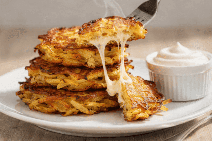 Crispy cheesy potato pancakes pulled apart with a fork showing stretchy melted cheese, served with a bowl of sour cream.