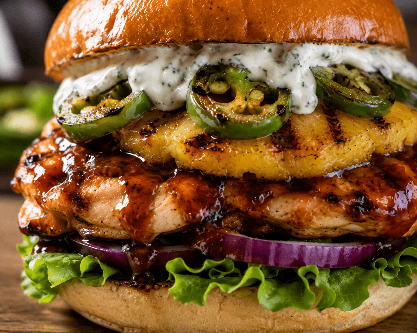 Extreme close-up of BBQ chicken pineapple burger showing grilled pineapple, jalapeños, creamy ranch sauce, and BBQ glazed chicken on brioche bun.