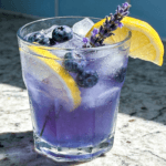 Close-up front view of Blueberry Lavender Lemonade with fresh blueberries, lemon slices, lavender sprigs, crushed ice, and chilled floral summer drink styling.