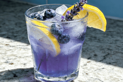 Close-up front view of Blueberry Lavender Lemonade with fresh blueberries, lemon slices, lavender sprigs, crushed ice, and chilled floral summer drink styling.