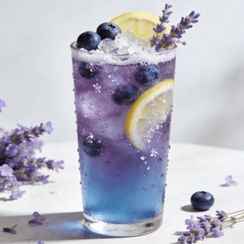 Zoomed-out front view of Blueberry Lavender Lemonade with fresh blueberries, lavender flowers, lemon slices, and icy floral lemonade served in a clear chilled glass.