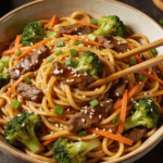 Top view of beef and broccoli lo mein noodles with sesame seeds, carrots, and green onions in savory stir fry sauce.