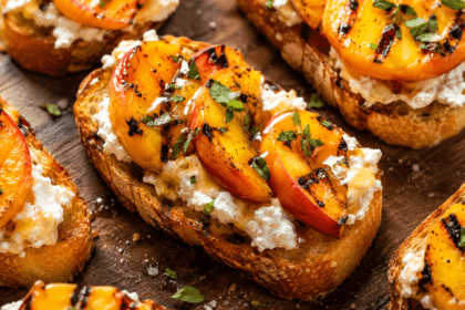 Close-up of grilled peach crostini with creamy goat cheese, honey drizzle, toasted bread, and fresh thyme garnish.