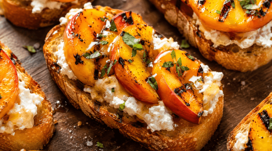 Close-up of grilled peach crostini with creamy goat cheese, honey drizzle, toasted bread, and fresh thyme garnish.