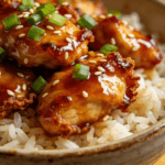 Close-up of honey sriracha chicken served over jasmine rice with sesame seeds and green onions in a ceramic bowl for a quick sweet and spicy chicken dinner.