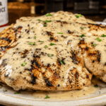 Front view of grilled chicken breasts covered in creamy Alabama white sauce on a rustic plate.