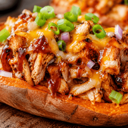 Close-up of a loaded sweet potato stuffed with grilled BBQ chicken, melted cheese, red onion, and green onions.