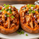 Front view of two BBQ chicken stuffed sweet potatoes topped with melted cheese, barbecue sauce, and green onions.
