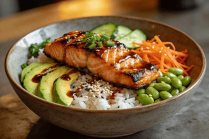 Front view of teriyaki salmon rice bowl with avocado, edamame, carrots, cucumber, and sesame seeds over jasmine rice.
