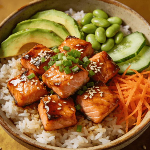 Top view of teriyaki salmon rice bowl with avocado, cucumber, edamame, carrots, sesame seeds, and green onions.