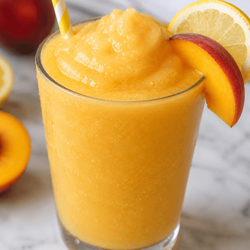 Close-up front view of frozen peach lemonade slush in a chilled glass with peach slices, lemon garnish, and icy blended summer drink texture.