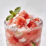 Close-up front view of a frozen watermelon coconut slushie topped with fresh watermelon cubes, coconut flakes, and mint in a chilled glass.