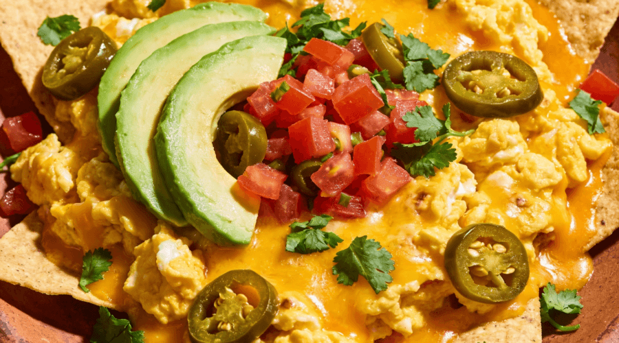 Top view of breakfast nachos with eggs cheese avocado tomatoes and jalapenos on a plate