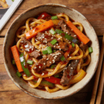 Top view of Korean beef noodle stir fry with vegetables and sesame garnish in savory sauce