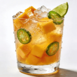 Close-up front view of a mango jalapeño sparkling cooler with fresh mango cubes, jalapeño slices, crushed ice, and sparkling bubbles in a chilled glass.