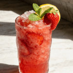 Close-up front view of Strawberry Mint Lemonade Cooler with fresh strawberries, mint leaves, lemon slices, crushed ice, and chilled summer drink styling.