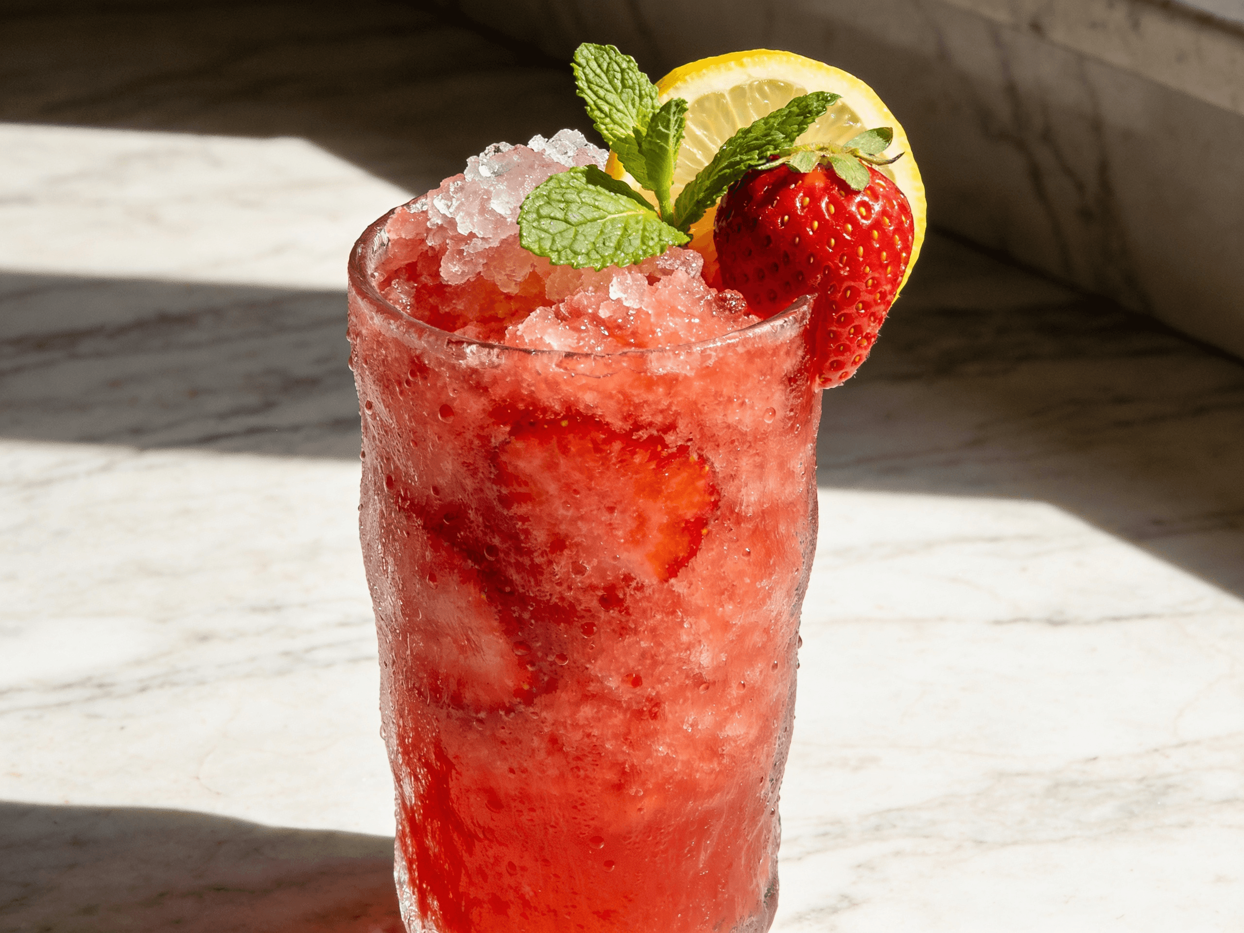 Close-up front view of Strawberry Mint Lemonade Cooler with fresh strawberries, mint leaves, lemon slices, crushed ice, and chilled summer drink styling.