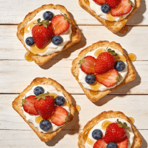 Top view of yogurt toast with berries and honey on crispy bread arranged on a wooden surface