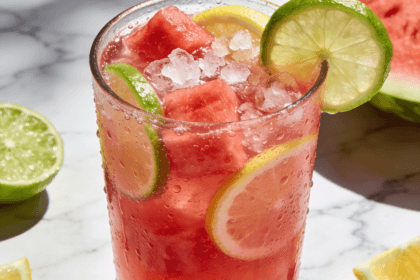 Close-up front view of Watermelon Lime Lemonade with fresh watermelon cubes, lime slices, lemon wedges, crushed ice, and chilled summer drink presentation.