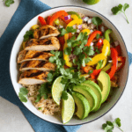 Top view of chicken fajita bowl with rice, grilled chicken, peppers, avocado, and lime