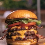 Front view of a BBQ bacon cheddar smash burger stacked with crispy beef patties, melted cheese, bacon, lettuce, and tomato.