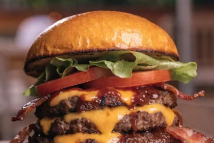 Front view of a BBQ bacon cheddar smash burger stacked with crispy beef patties, melted cheese, bacon, lettuce, and tomato.