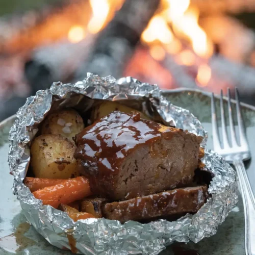 Front-view plated grilled BBQ meatloaf foil packet dinner with roasted vegetables and barbecue sauce.
