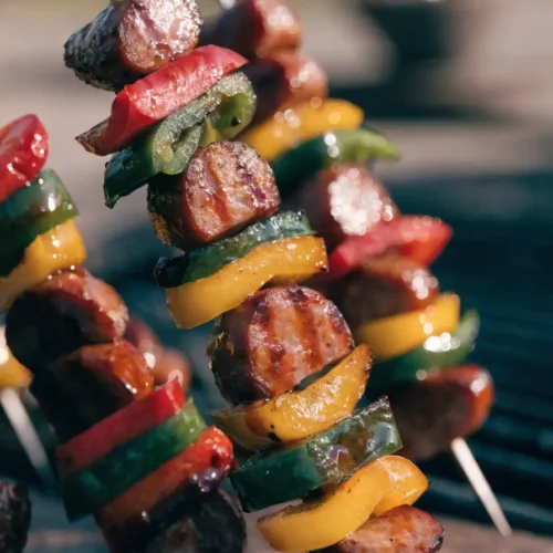 Close-up of grilled BBQ sausage and pepper skewers with colorful bell peppers, barbecue glaze, and charred grill marks.