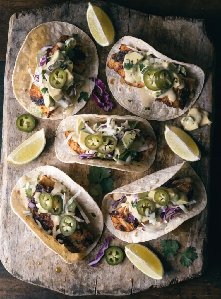 Overhead view of Cajun grilled fish tacos with avocado slaw, cilantro, jalapeños, and lime wedges.