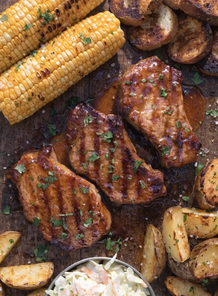 Top-view of maple Dijon pork chops arranged on a serving platter with fresh herbs and barbecue side dishes.