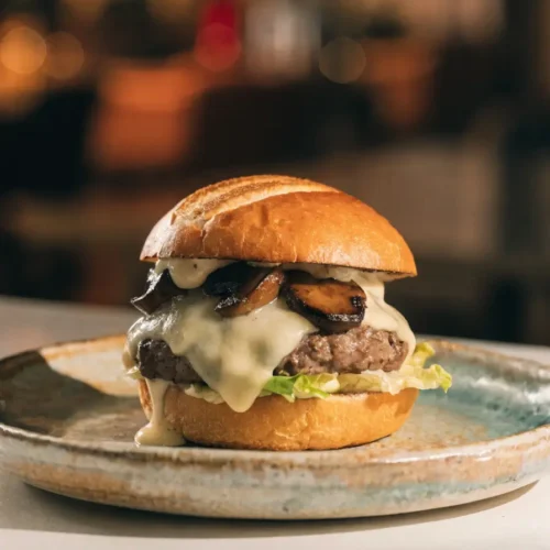 Front-view plated mushroom Swiss burger topped with grilled mushrooms, Swiss cheese, and garlic aioli.